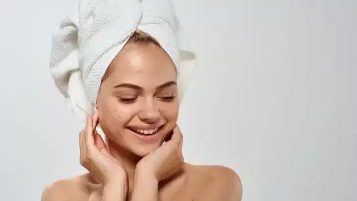 Smiling woman with acne wearing a towel on her head.