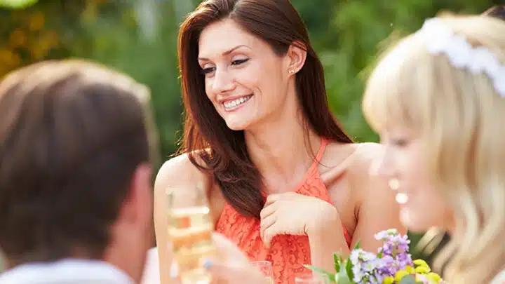 Close up of female guest at wedding wearing coral halter dress.