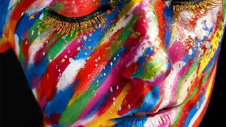 Close up view of woman wearing multicolored makeup all over her face to represent spring 2023 beauty trends.