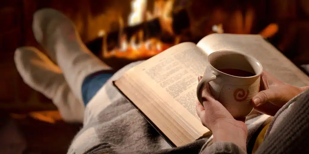Women lounging by the fire with a blanket and good book